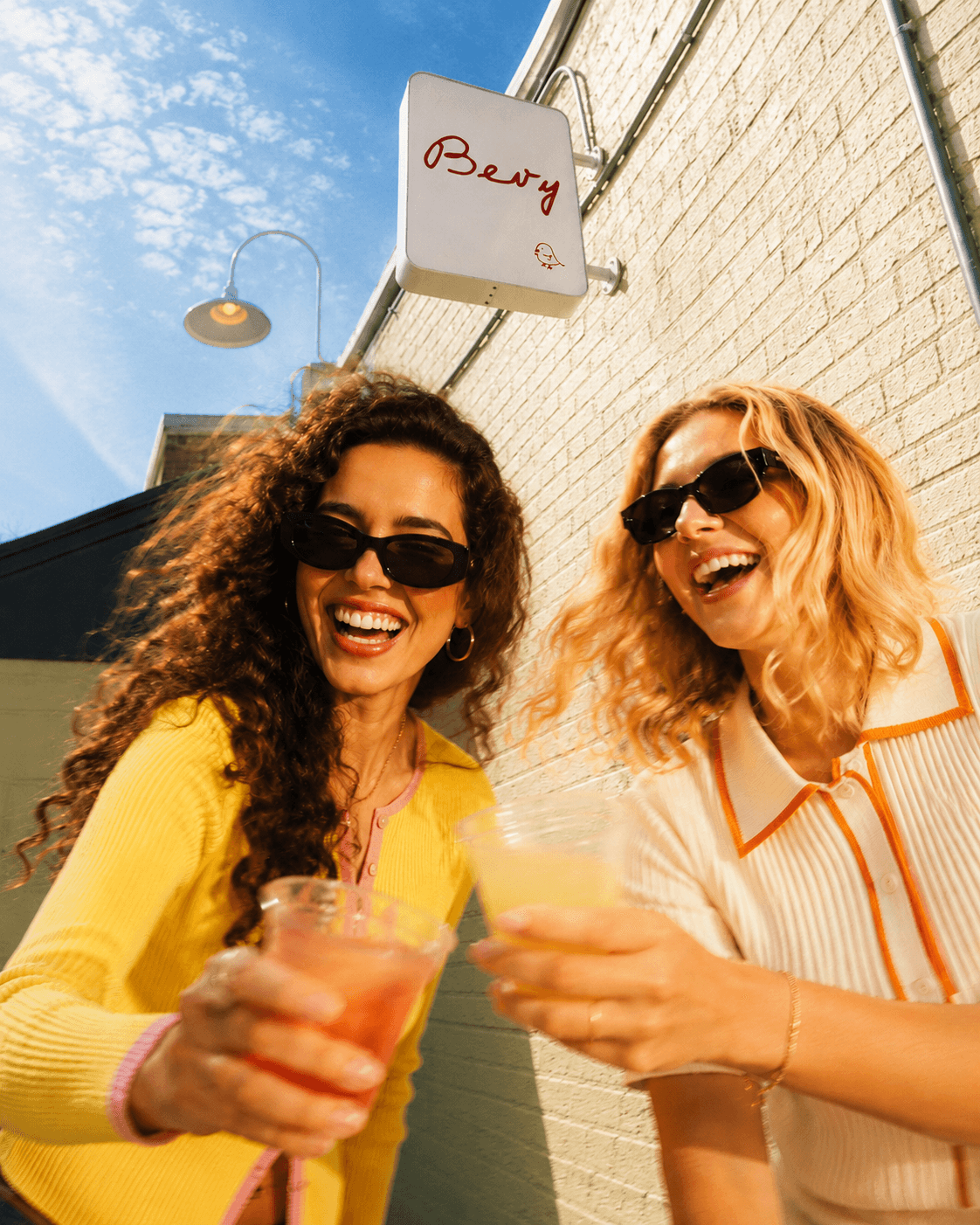 Two friends toasting under the Bevy sign on the Coop patio